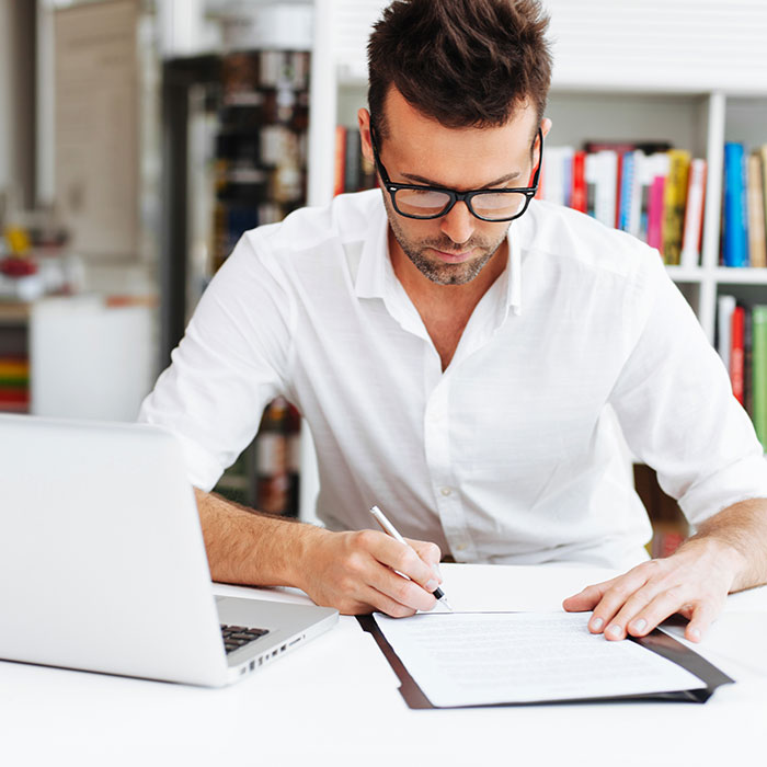 Junger Mann am weißen Schreibtisch mit MacBook und Notizen